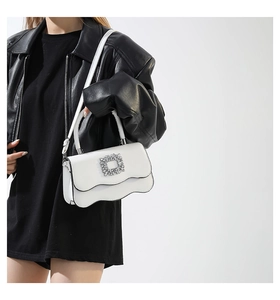 Détail du sac blanc à rabat ondulé avec grande boucle en strass sur une veste en cuir noir