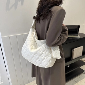 Close-up of white quilted tote bag with heart embroidery and wide shoulder strap detail