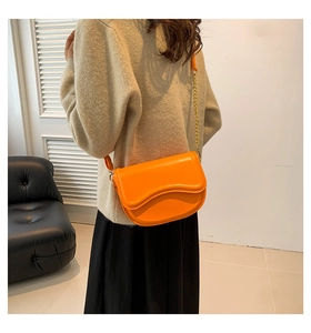 Detailed view of the wavy flap design and gold chain on this orange leather saddle bag