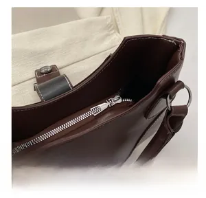 Detailed macro view of the smooth silver metal zipper and white contrast stitching on brown bag