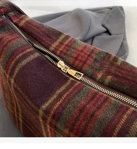 Detail of smooth gold metal zipper on red and green plaid textured fabric bag