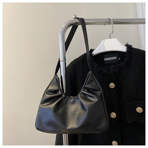 Detail of black pleated hobo bag in glossy PU leather hanging on a hanger