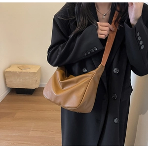 Détail d'un sac bandoulière marron en cuir grainé avec large sangle porté par un mannequin