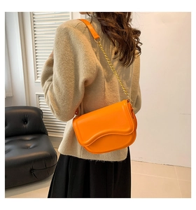 Detail of orange saddle bag with gold chain strap worn by model against a white wall