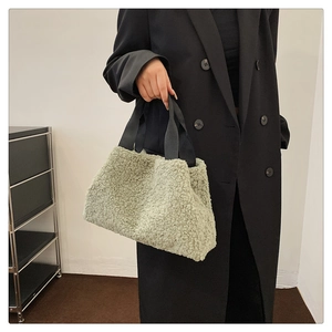 Close-up of fuzzy light green sherpa tote bag held by a model in a black suit