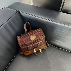 Close-up of red and green plaid wool backpack with brown leather trim and metal logo