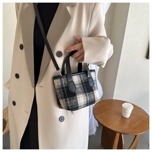 Detail of a mini plaid tote bag with wool texture and black leather strap in a cafe setting