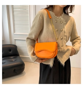 Model wearing a bright orange saddle bag with wavy edge and gold chain leather strap