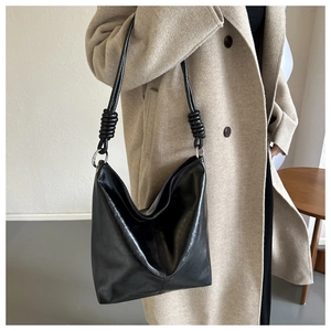 Detail of black leather tote bag featuring a knotted strap and silver metal ring