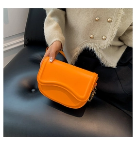 Detail of bright orange saddle bag with smooth leather finish and gold chain strap