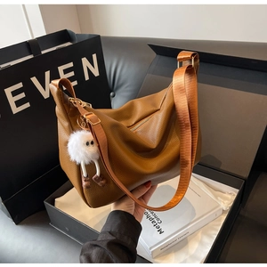 Détail du sac bandoulière en cuir caramel avec un pendentif monstre en peluche blanc