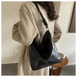 Detail of black leather tote bag with woven shoulder strap and metallic ring attachment