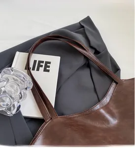 Close-up of vintage brown PU leather tote bag on grey suit with slim double handles