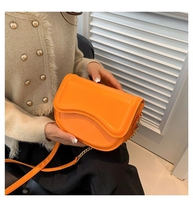 Detail of bright orange saddle bag with wavy flap and gold chain strap on model