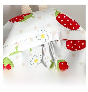 Detail of the white canvas backpack featuring red strawberry prints and drawstring closure