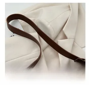 Detail of dark brown faux leather shoulder strap with fine stitching and gold metal ring