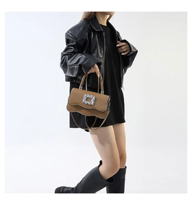 Sac bandoulière en cuir marron avec bord ondulé et boucle en cristal porté par mannequin