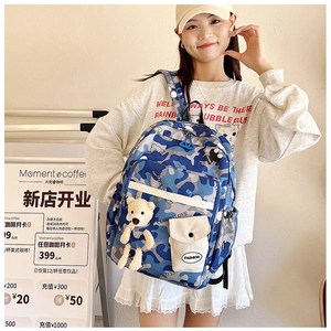 Detail showing blue camo backpack with white pocket, cat print and plush bear charm
