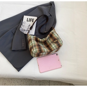 Flat lay of a green plaid hobo bag in wool fabric on a grey blazer showing texture
