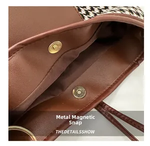 Detail view of the secure magnetic snap button closure on a brown plaid bucket bag