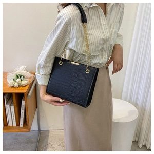 Close-up of black crocodile pattern tote bag with golden chain strap on a model