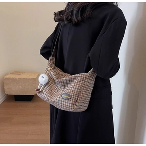 Detail of hobo bag in brown plaid fabric with leather label and plush charm