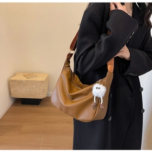 Détail d'un sac croissant en cuir litchi marron foncé avec un porte-clé peluche