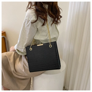 Detail of vintage black faux crocodile leather bag with gold chain strap worn by a model