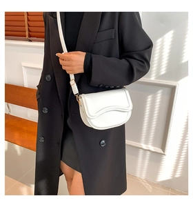 Detail of white leather saddle bag showing wavy edge design and gold metal buckle