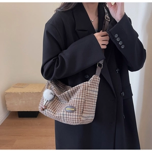 Detail of a brown plaid crossbody bag featuring a soft white fur ball charm and leather label
