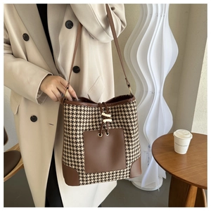 Detail view of houndstooth bucket bag with brown leather trim on a lifestyle model