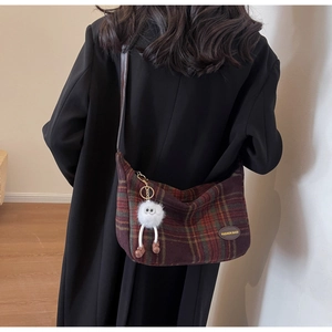 Detail of red and green plaid shoulder bag with plush pendant and leather brand tag