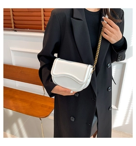 Close-up of a white minimalist saddle bag with gold chain strap and wavy flap detail