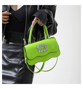 Détail du sac bandoulière vert à bords ondulés avec boucle en cristal sur cuir noir