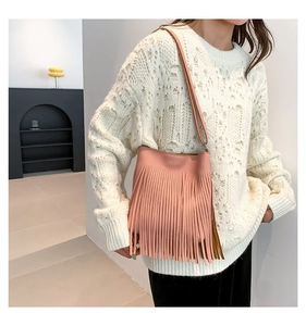 Pink fringed crossbody bag with pebble grain texture shown on a white knitted sweater