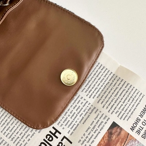 Close-up of dark brown leather flap featuring a round golden magnetic clasp on a retro bag