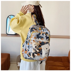 Detail showing high-capacity camouflage backpack with orange accents and plush bear charm