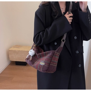 Detail of red and green plaid tweed crossbody bag with fur ball charm and leather strap
