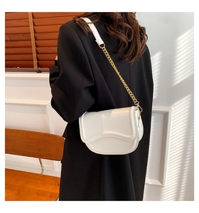 Detail of white saddle bag with wavy flap edge and gold chain strap on model