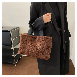 Close-up of brown plush fuzzy handbag with black straps held by model in black coat