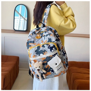 Detail of colorful camo backpack with orange accents and a cute plush bear charm