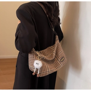 Close-up of brown plaid crescent bag with leather brand tag and plush monster charm