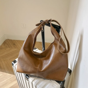 Vintage brown textured tote bag with adjustable strap placed on a white suitcase