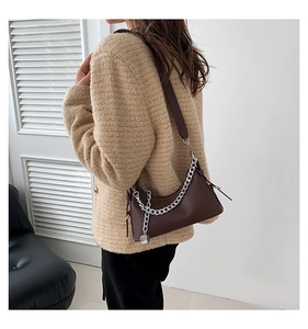 Détail du sac à bandoulière en cuir marron foncé avec chaîne argentée et pendentif en métal