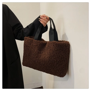 Detail of soft brown plush tote bag with black strap held by a model in a black suit