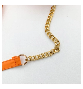 Macro detail of the orange lychee grain leather strap with gold chain link on white fabric