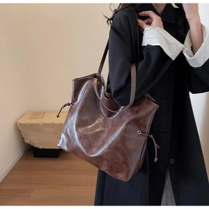 Detail of a brown glossy leather bucket bag showing the drawstring and shoulder strap