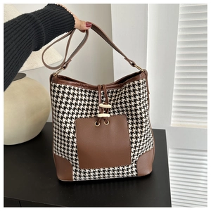 Detail of checkered houndstooth bucket bag featuring brown leather trim and drawstring closure