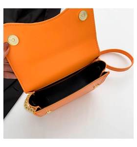 Detail of orange saddle bag showing gold magnetic closure and chain strap interior
