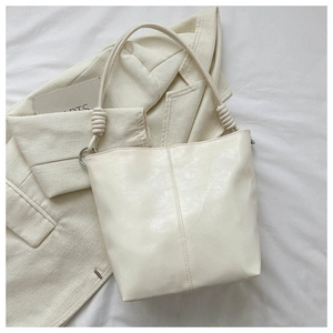 Detail of off-white bucket bag featuring a twisted knotted handle and vertical stitching